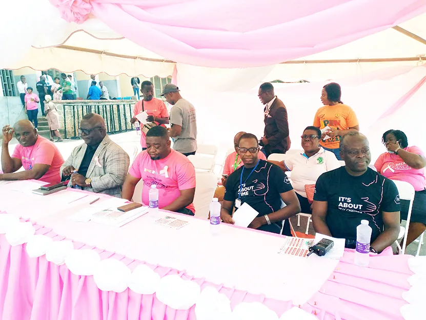 People seated at a pink-draped table under a pink canopy, several wearing pink breast cancer awareness T-shirts, at Effia Nkwanta Regional Hospital.