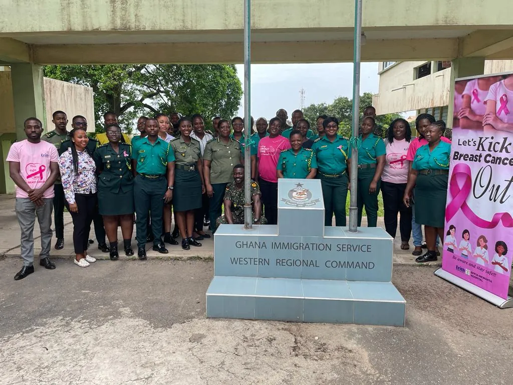 A large group of Ghana Immigration Service staff in uniform and Stepin team members in pink T-shirts pose beside a breast cancer awareness banner in Sekondi.